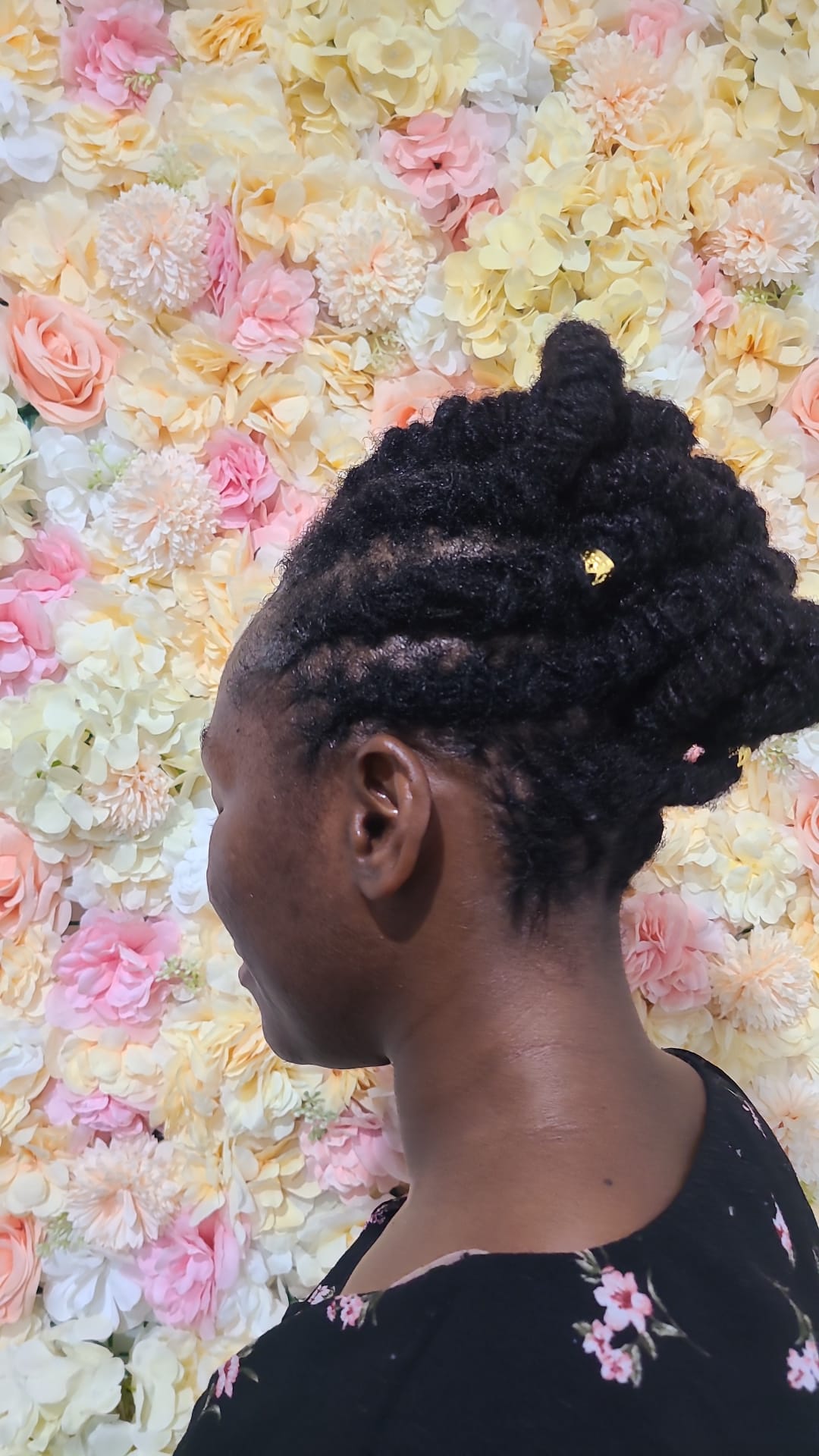 Loc updo with gold cuff against a floral wall